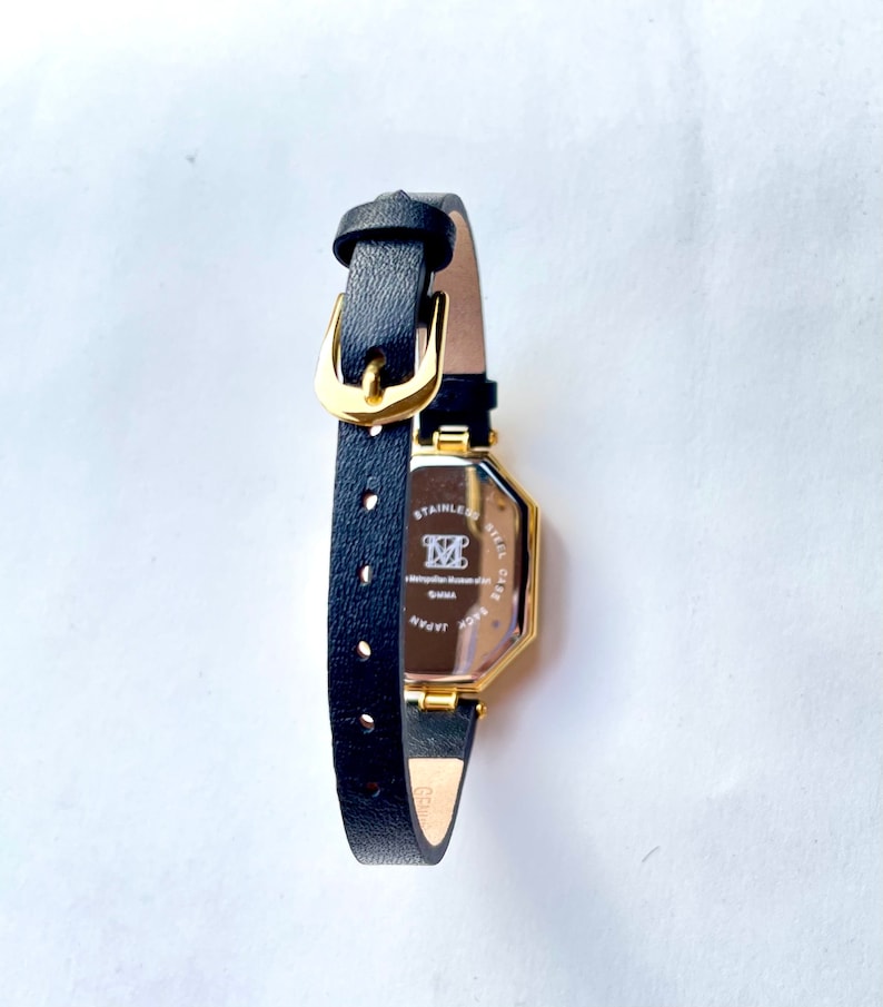 May include: A black leather watch with a gold-colored rectangular face. The watch has a black leather band with a gold buckle. The back of the watch has text that reads "STAINLESS STEEL CASE" and "JAPAN".