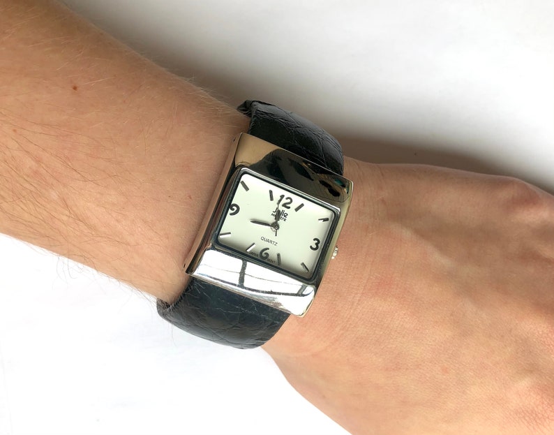 May include: A silver-toned rectangular watch with a white face and black leather band. The watch face displays the brand name "Zella Park" and the word "QUARTZ". The black band has a crocodile skin texture.