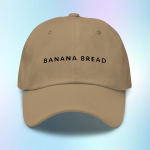 May include: A tan baseball cap with black embroidered text that reads "BANANA BREAD".