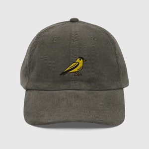 Könnte beinhalten: Eine dunkelgrüne Baseballkappe aus Cord mit einem gestickten gelben Vogelmotiv.