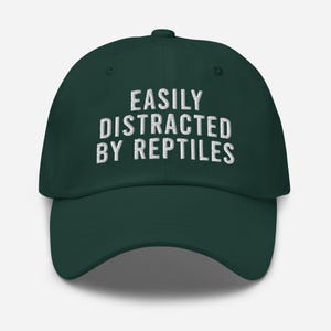 May include: A dark green baseball cap with white embroidered text that reads "EASILY DISTRACTED BY REPTILES".