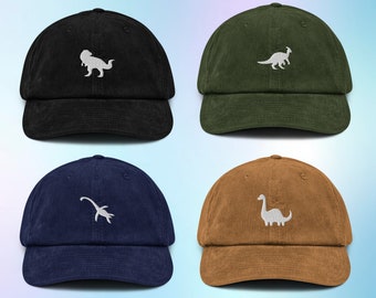 May include: Four corduroy baseball caps with different dinosaur silhouettes embroidered on the front. The caps are black, green, navy blue, and brown.