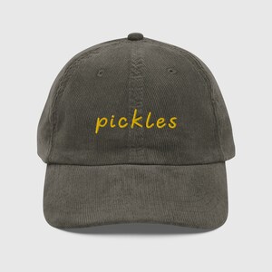 Op de afbeelding: Een donkergroene corduroy baseballpet met het woord "pickles" geborduurd in geel.