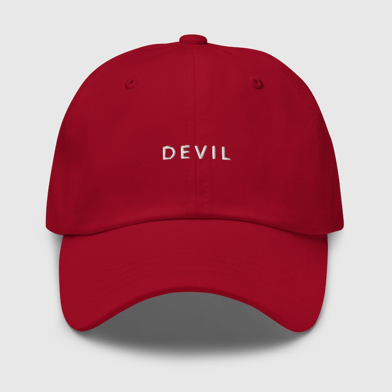 Pu&ograve; includere: Un cappello da baseball rosso con la parola "DEVIL" ricamata in bianco sul davanti.