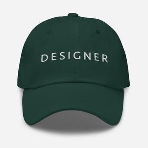 May include: A dark green baseball cap with the word "DESIGNER" embroidered in white on the front.