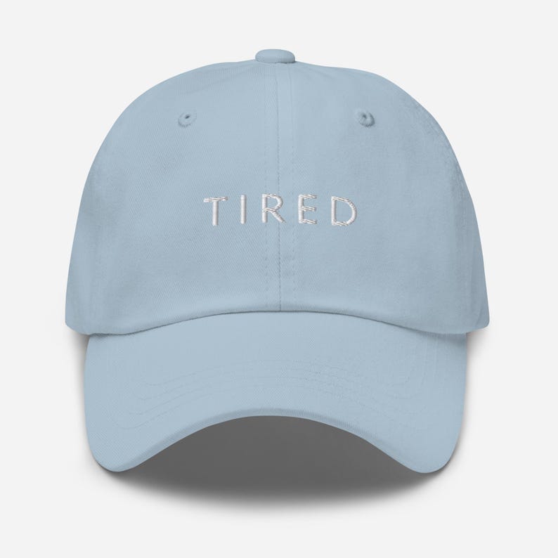 May include: A light blue baseball cap with the word "TIRED" embroidered in white on the front.