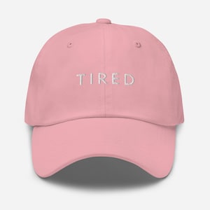 May include: A pink baseball cap with the word "TIRED" embroidered in white on the front.
