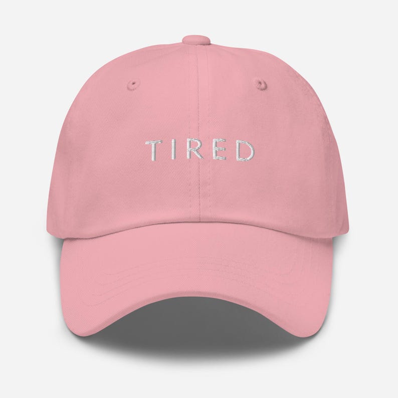 May include: A pink baseball cap with the word "TIRED" embroidered in white on the front.