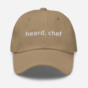 May include: A tan dad hat with the text "heard, chef" embroidered in white on the front.