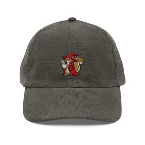 May include: A corduroy baseball cap in a muted green color. The cap features an embroidered design of a squirrel wearing a red wizard's hat and cloak, holding a coffee cup. The squirrel is brown and white.