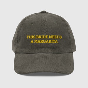 May include: A dark green corduroy baseball cap with the text "THIS BRIDE NEEDS A MARGARITA" embroidered in yellow.
