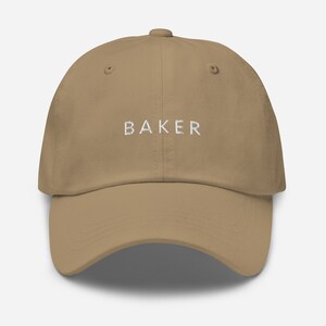 May include: A khaki dad hat with the word "BAKER" embroidered in white on the front.