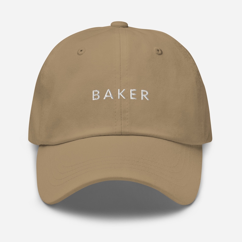 May include: A khaki dad hat with the word "BAKER" embroidered in white on the front.