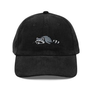 K&ouml;nnte beinhalten: Schwarze Cord-Baseballkappe mit einem gestickten Waschb&auml;r-Design in Grau und Wei&szlig;. Die Kappe hat einen gebogenen Schirm und einen verstellbaren Riemen. Ein modisches Accessoire f&uuml;r den Alltag.
