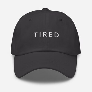 May include: A dark gray baseball cap with the word "TIRED" embroidered in white on the front.