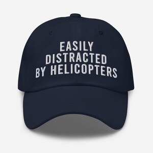 May include: A navy blue baseball cap with white embroidered text that reads "EASILY DISTRACTED BY HELICOPTERS".
