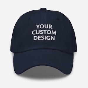 May include: A navy blue baseball cap with white embroidered text that reads "YOUR CUSTOM DESIGN".