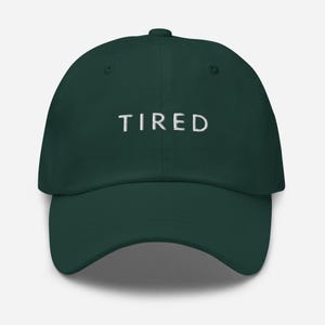 May include: A dark green baseball cap with the word "TIRED" embroidered in white on the front.