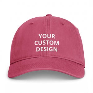 May include: A solid dark pink baseball cap with a six-panel construction and a curved brim. The front of the cap features the white text "YOUR CUSTOM DESIGN" printed in a clean, sans-serif font centred across the two front panels.