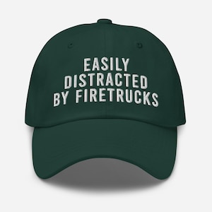 Op de afbeelding: Een donkergroene baseballpet met witte geborduurde tekst die "EASILY DISTRACTED BY FIRETRUCKS" luidt.