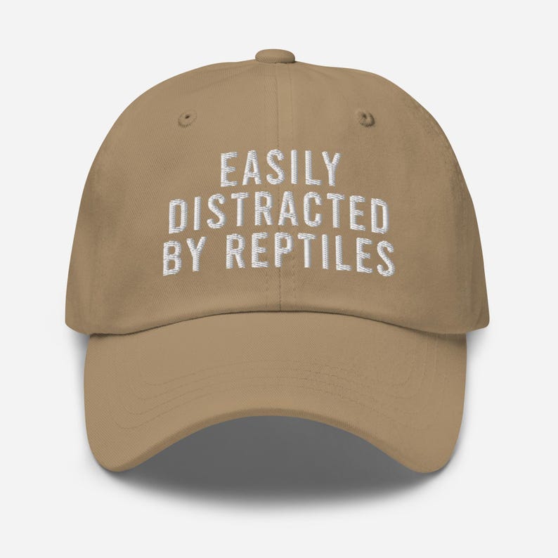 May include: A tan baseball cap with white embroidered text that reads "Easily Distracted By Reptiles".