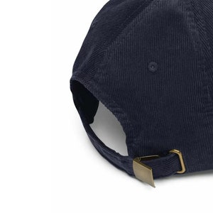 K&ouml;nnte beinhalten: Marineblaue Cord-Baseballkappe mit gebogenem Schirm und verstellbarem Riemen. Die Kappe hat eine messingfarbene Metallschnalle zur Gr&ouml;&szlig;enanpassung. Der Cordstoff hat eine vertikale Rippenstruktur.