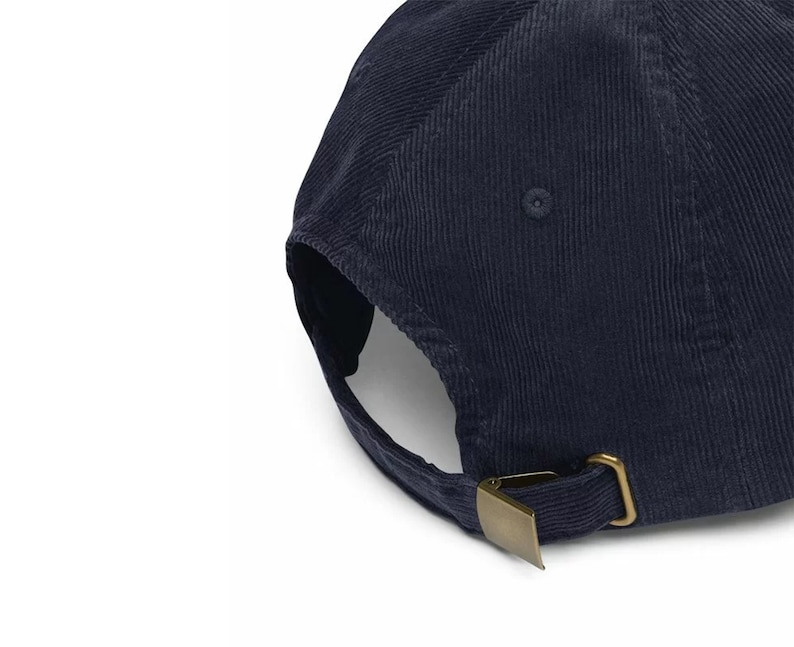 K&ouml;nnte beinhalten: Marineblaue Cord-Baseballkappe mit gebogenem Schirm und verstellbarem Riemen. Die Kappe hat eine messingfarbene Metallschnalle zur Gr&ouml;&szlig;enanpassung. Der Cordstoff hat eine vertikale Rippenstruktur.