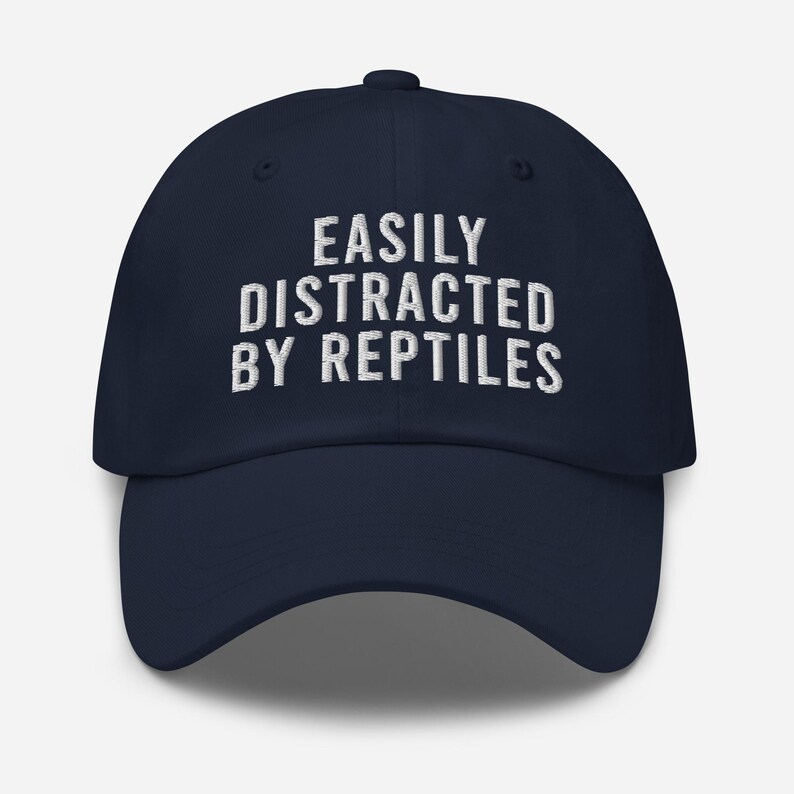 May include: A navy blue baseball cap with white embroidered text that reads "EASILY DISTRACTED BY REPTILES".
