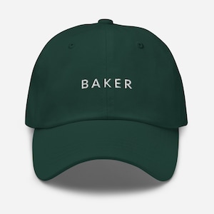 May include: A dark green baseball cap with the word "BAKER" embroidered in white on the front.
