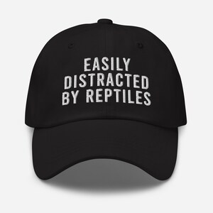 May include: Black baseball cap with white embroidered text that reads "Easily Distracted By Reptiles".