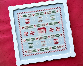 Puede incluir: Un bordado de punto de cruz cuadrado en un marco blanco festoneado con fondo azul claro. El diseño incluye filas de motivos navideños rojos y verdes, que incluyen tazas, caramelos de menta y un icono central de la cara de Santa Claus.