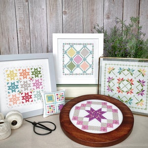 May include: Four framed cross-stitch embroidery projects with a variety of colorful geometric patterns. The projects are displayed on a wooden surface with a spool of white thread and a pair of scissors.