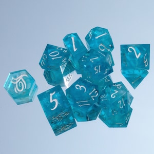 Puede incluir: Un conjunto de diez dados de color azul turquesa con números blancos. Los dados están esparcidos sobre una superficie azul claro.