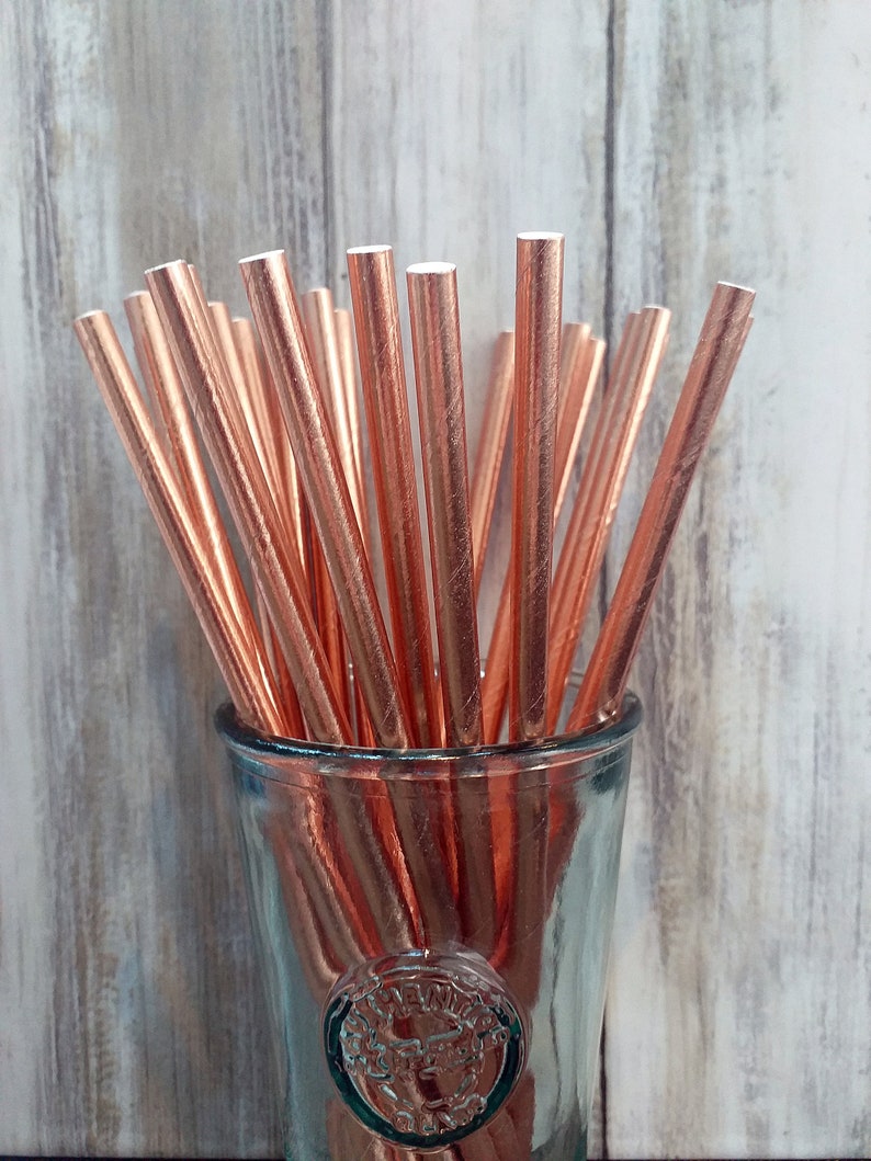 Op de afbeelding: Een glazen pot gevuld met roosgoud papier rietjes. De rietjes zijn in een waaier vorm gerangschikt en zijn allemaal even groot.