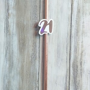 Op de afbeelding: Een roosgoud drinkrietje met een witte sticker waarop "21" staat.