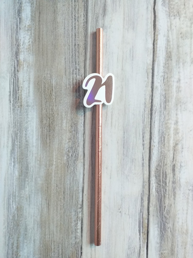 Op de afbeelding: Een roosgoud drinkrietje met een witte sticker waarop "21" staat.