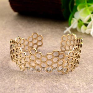Könnte beinhalten: Goldfarbenes Metallarmband mit einem Wabenmuster. Das Armband ist offen und verstellbar.
