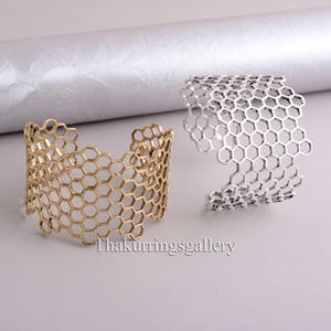 Könnte beinhalten: Zwei Metallarmbänder mit einem Wabenmuster. Ein Armband ist golden und das andere ist silber.