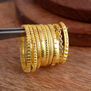 Puede incluir: Un conjunto de diez anillos apilables de color dorado con diferentes patrones texturizados. Los anillos están apilados uno encima del otro y dispuestos en un patrón circular.
