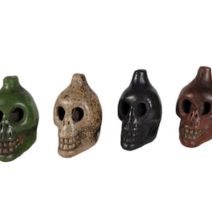 May include: Four ceramic skull shaped bottle stoppers in green, beige, black, and brown.