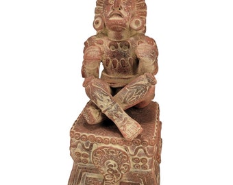 May include: A terracotta-colored sculpture of a seated figure with crossed legs. The figure has detailed facial features, ornate headdress, and decorative patterns on the chest and legs. The sculpture is seated on a square base with carved designs.