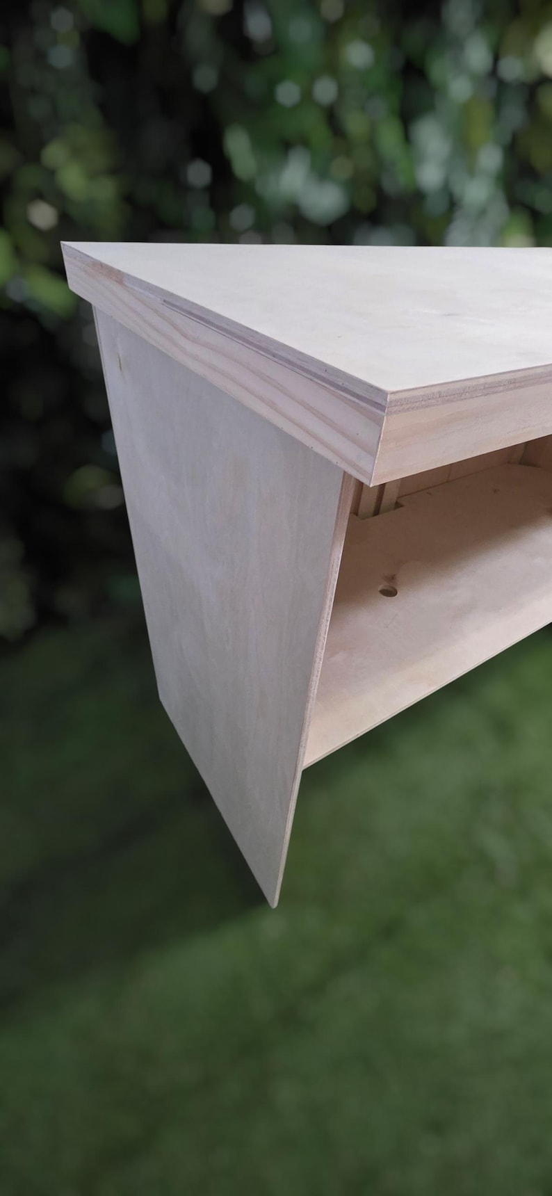 May include: A light-colored, unfinished wooden bench with a simple, modern design. The bench features a flat top and a lower shelf, with angled legs. The wood appears to be plywood. The bench is suitable for indoor or outdoor use.