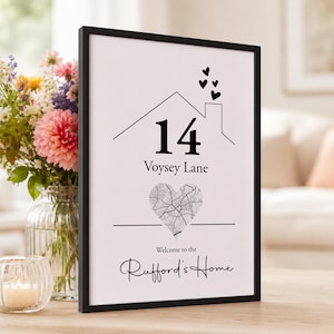 Puede incluir: Una impresión enmarcada con un dibujo de líneas negras de una casa con el número 14, el texto Voysey Lane, un mapa en forma de corazón y el texto Welcome to the Rufford's Home. El diseño incluye cuatro pequeños corazones negros sobre la chimenea.
