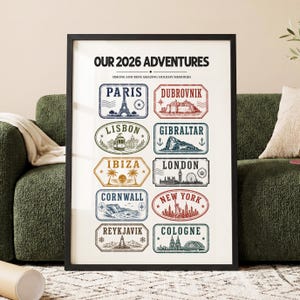 以下が含まれることがあります： 「OUR 2026 ADVENTURES」のテキストと、パリ、ロンドン、ニューヨークなどの都市のイラストが描かれた、額入りの旅行ポスター。 各都市は、色付きのバッジ内のユニークなイラストで表現されています。 ポスターはニュートラルな背景に表示されます。
