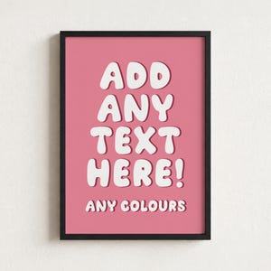May include: A rectangular wall art print in a black frame featuring a pink background with the white text ADD ANY TEXT HERE! and the smaller white text ANY COLOURS below it. The letters have a rounded, bubble-like font style with a drop shadow.