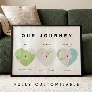 May include: A framed print featuring the words "OUR JOURNEY" above three heart-shaped maps. Each map has a red heart and dates for key events. The text "FULLY CUSTOMISABLE" is at the bottom. The print is displayed on a green sofa.