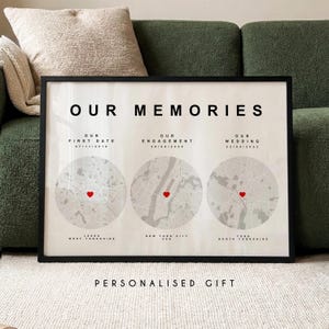 Può includere: Una stampa incorniciata con la scritta "OUR MEMORIES". Presenta tre illustrazioni di mappe circolari con indicatori a forma di cuore rosso, che rappresentano date e luoghi importanti: primo appuntamento, fidanzamento e matrimonio. Il testo in basso recita "PERSONALISED GIFT".