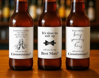 Könnte beinhalten: Drei Bierflaschen aus Braunglas mit weißen Etiketten. Das erste Etikett lautet: I could have said this over a beer but she made me give you this... will you be my Groomsman? Das zweite: It's time to suit up, Best Man? Das dritte: There will be... beers speeches and tears, will you be my Groomsman?