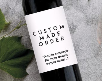 以下が含まれることがあります： 「CUSTOM MADE ORDER」と書かれた白いラベルが付いた黒いワインボトル。ラベルには「Please message for more details before order :)」というテキストも含まれています。緑の葉とグラスが背景にあります。