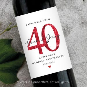 May include: A wine bottle with a white label featuring the text PAIRS WELL WITH, the number 40 in a red glitter-effect print, the names Anna & Jerry in black script, and the text HAPPY RUBY WEDDING ANNIVERSARY 1985-2025 with a small red heart.